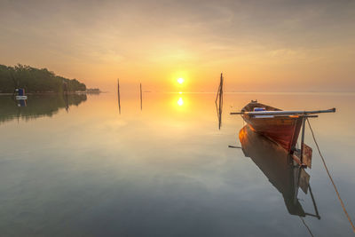 Sailboats moored in lake against sky during sunset