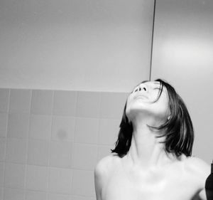 Shirtless woman with eyes closed in bathroom against wall at home