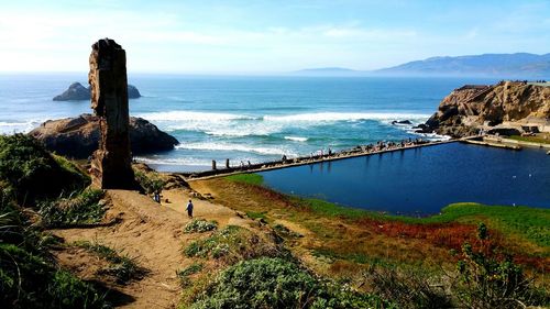 High angle view of old ruins and people walking on shore by sea against sky