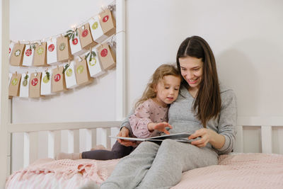 Mather with toddler child reading book or photo album on christmas eve near eco advent calendar