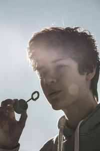 Close-up portrait of young man holding camera against sky