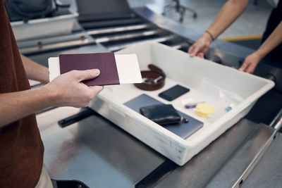 Passenger holding passport against personal items, liquids, and laptop in container at airport.