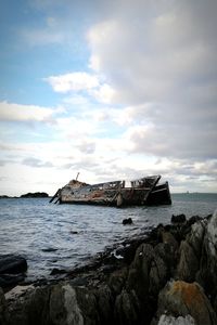 Scenic view of shipwreck on rocks against sea and sky