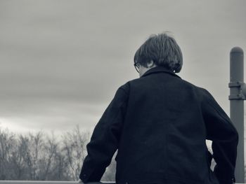 Rear view of man standing against cloudy sky