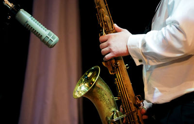 Midsection of male musician playing saxophone by microphone