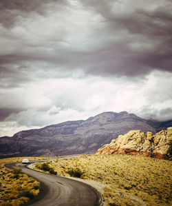 Road leading towards mountains against cloudy sky