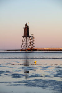 Lighthouse on sea against sky during sunset