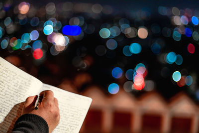 Cropped image of author writing in book against illuminated background