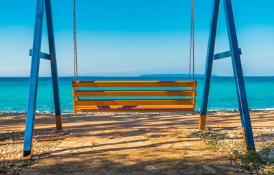 Empty swing on beach against sky