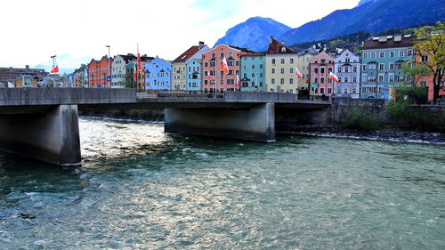 Bridge over river by buildings against sky