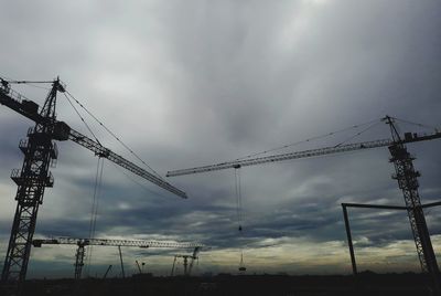 Low angle view of cranes at construction site against sky