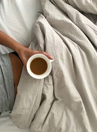 Midsection of woman holding coffee cup on bed