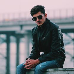 Portrait of young man sitting in city against sky