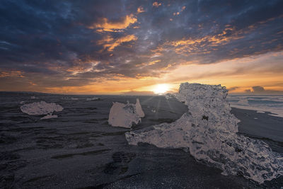 Close-up of iceberg chunk on black sand of diamond beach against sky at sunset