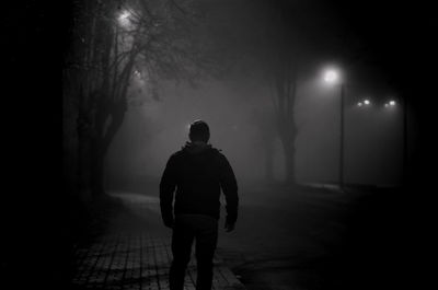 Rear view of man walking on footpath at night