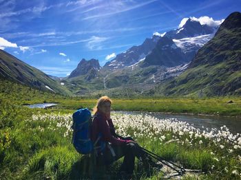 Smiling woman with backpack sitting against mountains