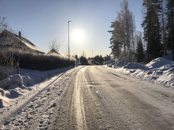 Snow covered road amidst trees against sky during winter