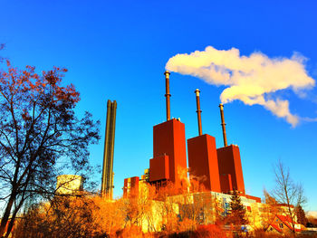 Low angle view of smoke emitting from factory against blue sky