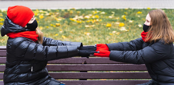 Women wearing mask holding hands against bench at park