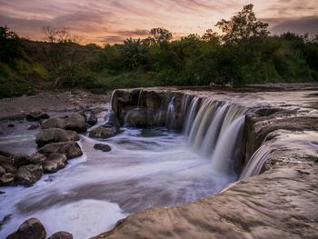 Scenic view of waterfall against sky during sunset