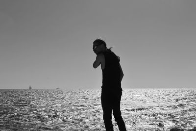 Young man standing by sea against clear sky