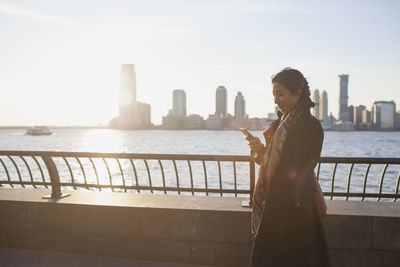 Young asian businesswoman looking at her smartphone standing on river promenade