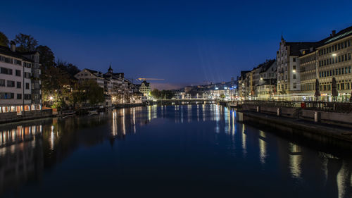 Illuminated buildings by river against sky at night