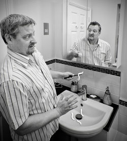 Digital composite of scared man looking at his angry reflection in bathroom