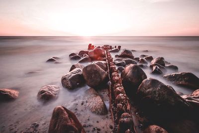Rocks on beach against sky during sunset