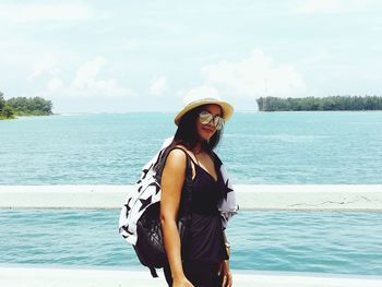 Portrait of smiling woman wearing sunglasses while standing against sea at beach