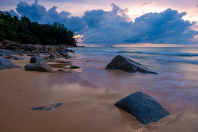 Rocks on beach against sky during sunset