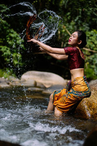 Side view of young woman splashing wet cloth in river