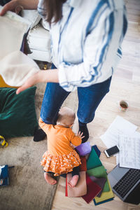 High angle view of daughter playing between working mother's legs in living room