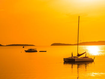 Silhouette of sailboat in sea against orange sky