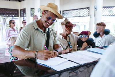 Happy man filling form at resort reception desk during vacation