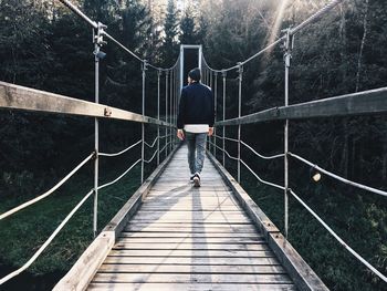 Rear view of man walking on footbridge against trees