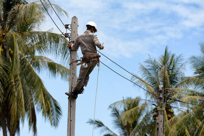Low angle view of man working on electric pole against sky