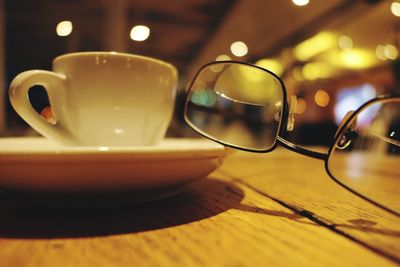 Close-up of eyeglasses with coffee cup on wooden table