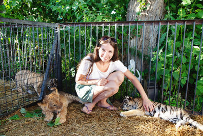 Portrait of young woman sitting on grassy field with tiger and lion babies 