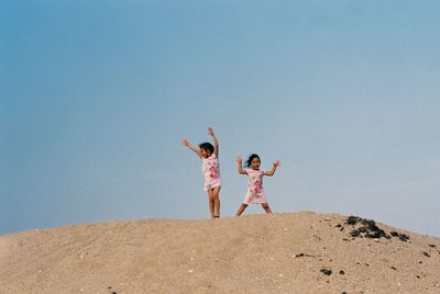 Siblings on sand at beach against clear sky