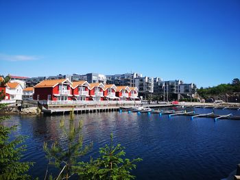 Buildings by river against clear blue sky