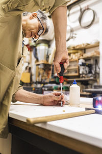 Mature male craftsperson using screwdriver on plank at workshop