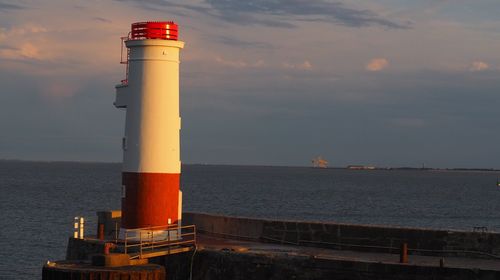 Lighthouse by sea against sky during sunset