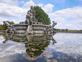 Statue in lake against cloudy sky