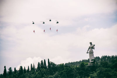 Low angle view of helicopters flying with flags by statue against sky