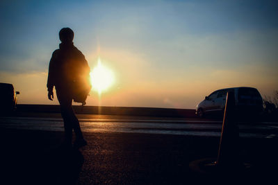 Rear view of silhouette person walking on road against sky during sunset