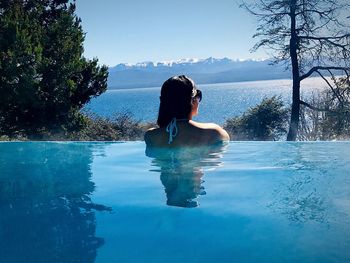 Rear view of woman swimming in infinity pool