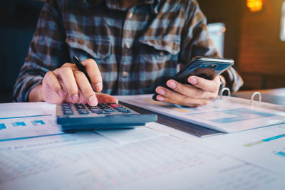 Midsection of businessman using calculator and mobile phone in office