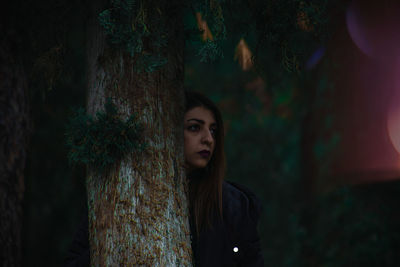 Portrait of young woman standing by tree in forest