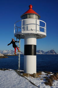 Full length of woman standing by lighthouse on snow covered mountain
